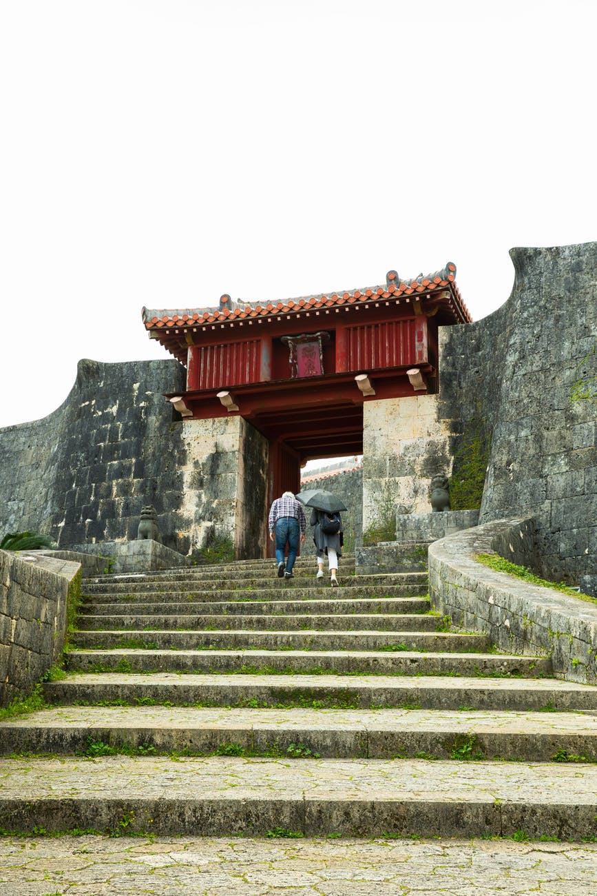 anonymous travelers climbing up stairs near shuri castle